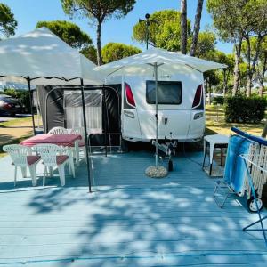une caravane blanche avec une tente, des tables et des chaises dans l'établissement WMC BUSCHMANN camping-in-venedig Wohnwagenvermietung at UNION LIDO Cavallino, à Cavallino-Treporti