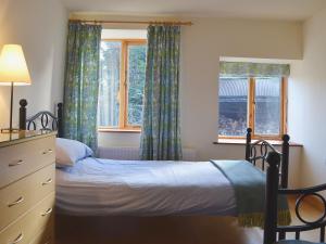 a bedroom with a bed and a dresser and two windows at Granary Cottage in Oswestry