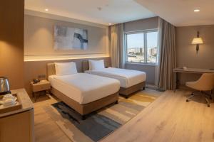 a hotel room with two beds and a desk and a window at Kolin Hotel Spa & Convention Center in Canakkale