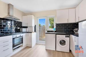 a kitchen with white cabinets and a washer and dryer at OnSiteStays - Comfortable Contractor Accommodation, 3-BR House, WIFI, Parking & Large Garden in Enfield Lock