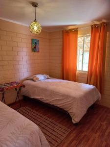 a bedroom with two beds and a window with orange curtains at Cabaña valle de elqui horcon Encantó del pimiento in Horcon