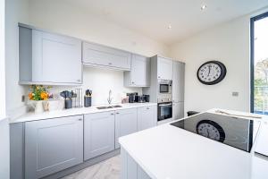 una cocina con armarios blancos y un reloj en la pared en Luxurious 4-Bedroom Penthouse: 15 Mins to City Centre, Secure Parking en Leeds