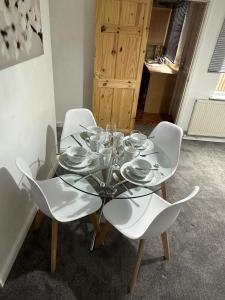 uma mesa de vidro com cadeiras brancas e pratos em Cosy Nest Getaways em Hickleton