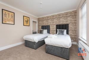 2 Betten in einem Zimmer mit Ziegelwand in der Unterkunft OnSiteStays - Stylish 4 BR House with Beautiful Outdoor Space, Wi-Fi & Smart TVs in Dartford