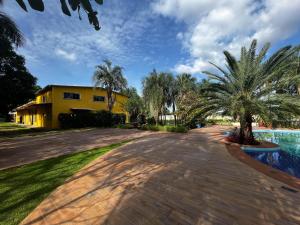 a driveway leading to a yellow house with palm trees at Villa Marina Casa de eventos in Senador Canedo