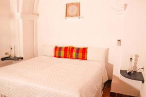 um quarto branco com uma cama com uma almofada colorida em La Casa de Mamapán Hotel Colonial Ahuachapan em Ahuachapán