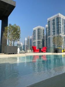 a pool with red chairs in front of a city at Modern 2BR and maid room with big terrace city walk in Dubai