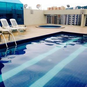 a swimming pool with two white chairs next to a building at Flat São Vicente 5 minutos da praia in São Vicente