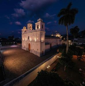 a large white building with a palm tree at night at La Casa de Mamapán Hotel Colonial Ahuachapan in Ahuachapán