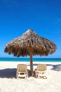 two chairs under a straw umbrella on a beach at Los Corales Beach Village Punta Cana - The original in Punta Cana