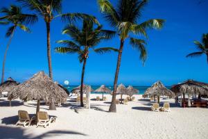 a beach with straw umbrellas and chairs and palm trees at Los Corales Beach Village Punta Cana - The original in Punta Cana