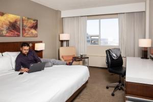 埃德蒙頓的住宿－三角洲艾德南酒店和和會議中心，一个人躺在一张床上,在旅馆房间里拿着笔记本电脑
