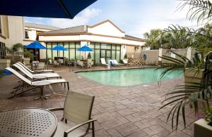 einen Pool mit Stühlen, Tischen und blauen Sonnenschirmen in der Unterkunft Holiday Inn Express and Suites New Orleans Airport, an IHG Hotel in Saint Rose