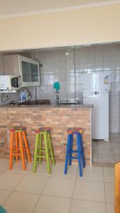 a kitchen with three colorful stools in front of a counter at Frente Mar - Apartamento para 4 Hóspedes com Home Office Wi-Fi 200mbps, Ar Condicionado e Cozinha Completa in São Vicente