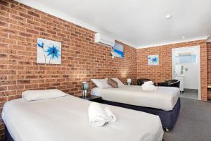 a room with two beds and a brick wall at Lake Macquarie Motor Inn in Belmont