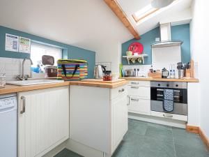 a kitchen with white cabinets and blue walls at Swallow Cottage in Llandwrog