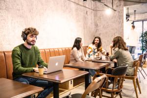 a group of people sitting at tables in a restaurant with a laptop at Ten to Ten Hostel in Sapporo