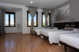 a room with four beds with windows and wooden floors at Hostal Venta de Valcorba in Soria