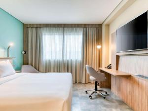 um quarto de hotel com uma cama, uma secretária e uma televisão em Novotel BH Savassi em Belo Horizonte