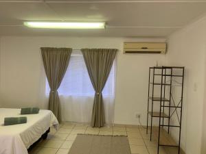 - une chambre avec un lit et une fenêtre avec des rideaux dans l'établissement Pioneerspark Self Catering, à Windhoek