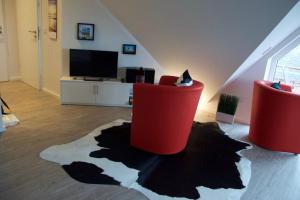 a living room with two red chairs and a tv at Bootshaus SunDeck - Strandnah in den Dünen in Wangerooge