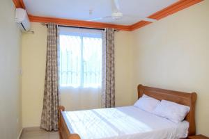 Schlafzimmer mit einem Bett und einem Fenster mit Vorhängen in der Unterkunft Millan Homes in Mombasa