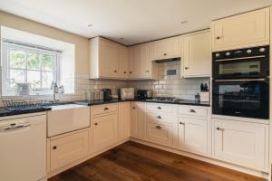 a kitchen with white cabinets and black appliances at Yew Tree: Historic Georgian Farmhouse, Ellonby in Ellonby