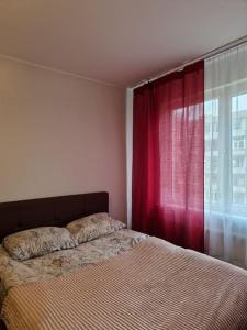 a bedroom with a bed and a window with red curtains at Iļģuciema Apartment in Rīga