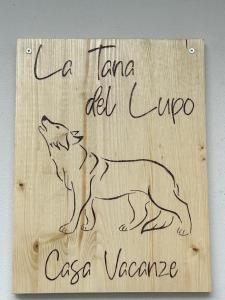 un cartel de madera con un dibujo de un perro. en La tana del lupo, en Camporosso in Valcanale