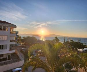 een zonsondergang boven de oceaan en een gebouw met palmbomen bij Apartamento pe na areia e com vista linda in Florianópolis