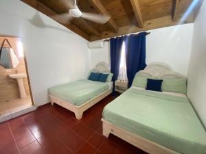 バヤイベにあるApartamentos Magallanes Bayahibeのベッド2台、青いカーテン付きの窓が備わる客室です。