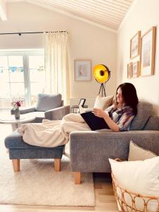 una mujer sentada en un sofá leyendo un libro en Strandzone 29 en Kronsgaard