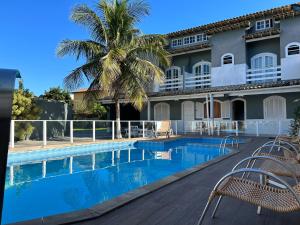 a resort pool with chairs and a palm tree at Suítes Moinho in Cabo Frio