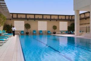 une personne debout à côté d'une grande piscine dans l'établissement Courtyard By Marriott Kuwait City, à Koweït