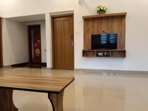 a living room with a table and a tv on a wall at JJ HOLIDAY HOMES WAYANAD in Kalpetta