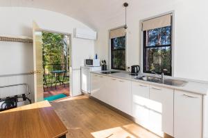 a kitchen with white cabinets and a table and some windows at Nambucca Valley Train Carriages in Nambucca +23 photos