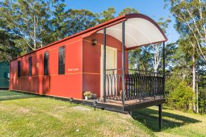 a red house with a balcony in a field at Nambucca Valley Train Carriages in Nambucca