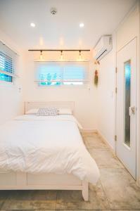 a white bedroom with a white bed and a window at Jeju Love Stay Purple in Jeju