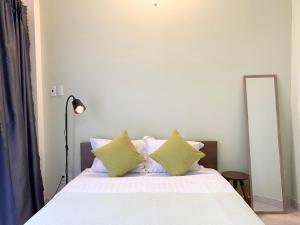 1 cama con sábanas blancas y almohadas verdes junto a un espejo en Acorn Saigon Hotel - Bui Vien en Ho Chi Minh