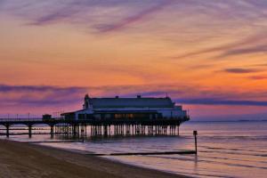 a pier with a building on the beach at sunset at Coastal Views Apartment Cleethorpes in Cleethorpes