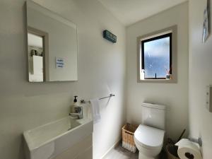 a bathroom with a toilet and a sink and a window at Hahei Ocean's 76 in Hahei
