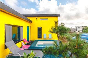 a yellow house with a swimming pool and chairs at Jeju Love Stay Yellow in Jeju