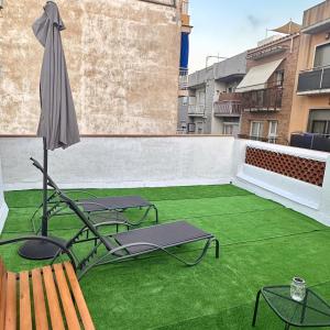 eine Terrasse mit grünem Gras, einem Sonnenschirm und Stühlen in der Unterkunft CozyCatalonia - Exclusive Attic in Central Blanes in Blanes