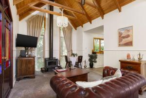sala de estar con sofá de cuero y TV en Harem Cottage Gembrook - Spa Bath & Wood Fireplace en Gembrook