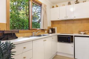 cocina con armarios blancos, fregadero y ventana en Harem Cottage Gembrook - Spa Bath & Wood Fireplace en Gembrook