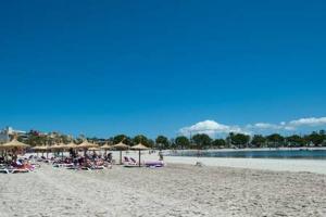 einen Strand mit Stühlen und Sonnenschirmen und Menschen darauf in der Unterkunft Oleanda in Port d'Alcúdia