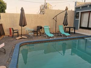 una piscina con sillas, mesas y sombrillas en Phindulo Bed and Breakfast - No Loadshedding, Smart TVs & unlimited free fibre wifi, en Krugersdorp