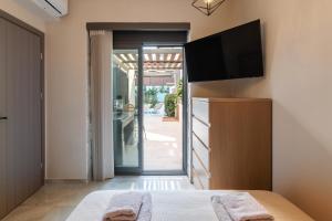 ein Schlafzimmer mit einem Bett, einem TV und einer Glasschiebetür in der Unterkunft Domenica Diamond Villas in Chaniotis