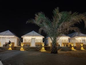 a couple of white tents with a palm tree at night at Desert Heritage Resort & Camps in Jaisalmer