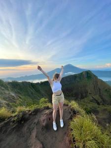 a woman standing on top of a mountain with her arms up at Batur Caldera Guesthouse in Kintamani